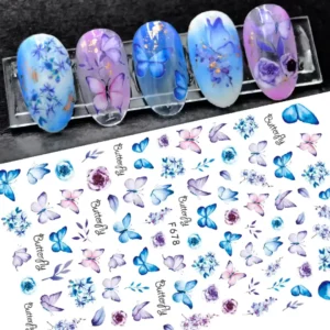 Planche de stickers Nail Art professionnels motif papillons et fleurs aquarelles bleus et violets référence F 678, présentée à côté de capsules d'exposition affichant des dégradés artistiques décorés de papillons et d'éclats de feuilles d'or, Cosminty La Réunion.